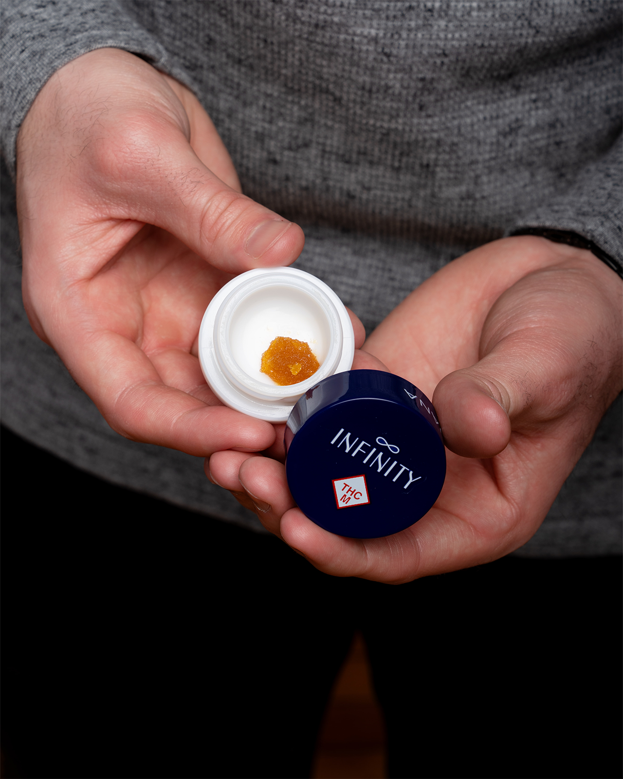 A man holds an open jar of infinity with wax inside.