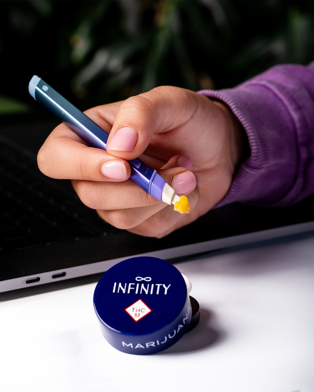 A hand holds a hot knife pen with a dollop of live wax on it. Below is an infinity jar