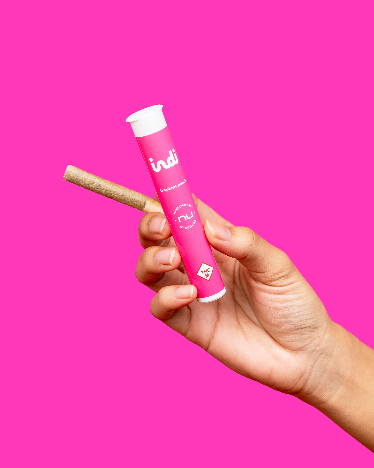 A hand holds an Indi pre-roll with the Tropical Punch pre-roll packaging.