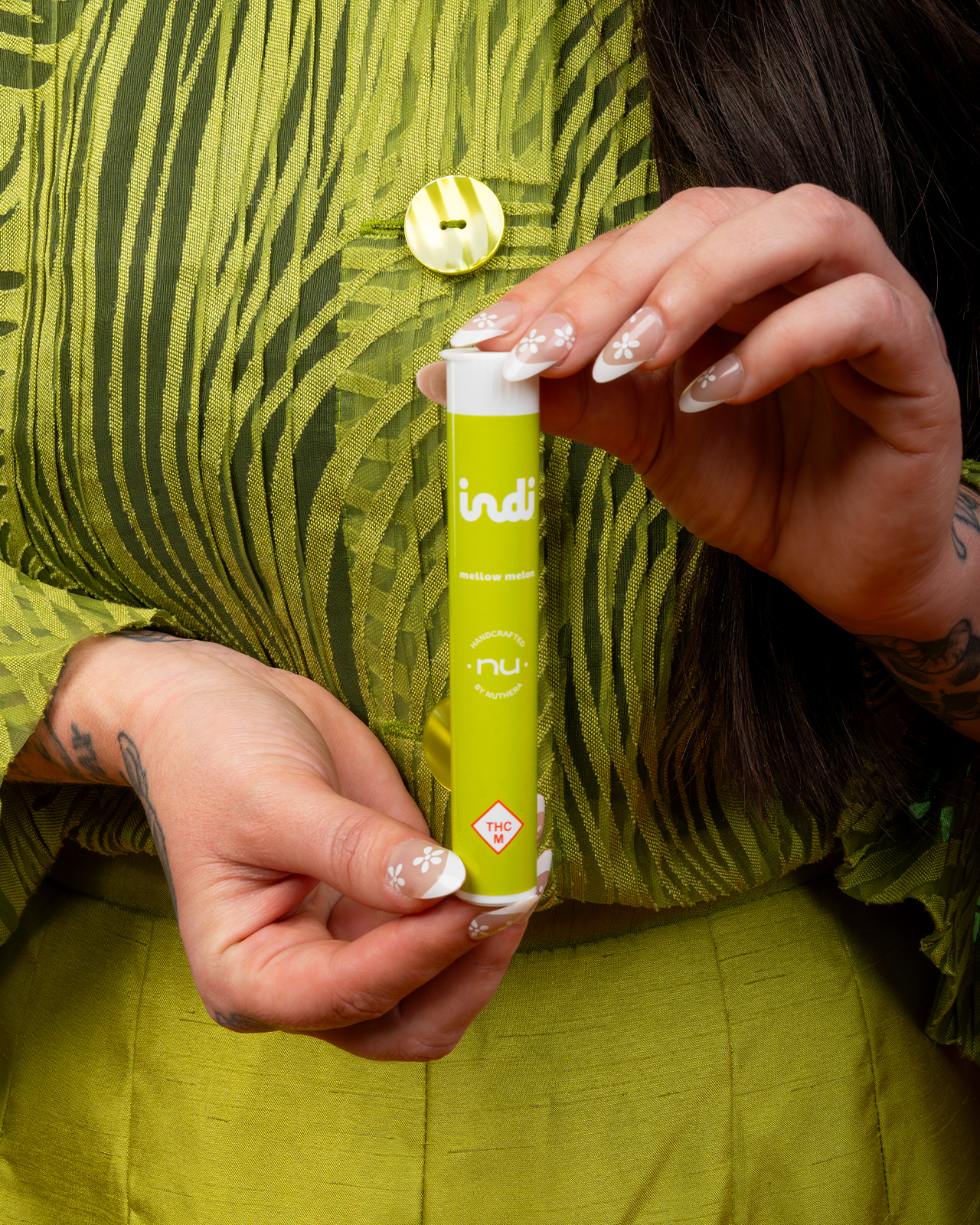 A woman with long nails holds a tube of a Mellow Melon Indi pre-roll, and her clothes are the same neon green.